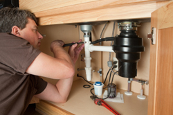 Tom is under the sink repairing a garbage disposal